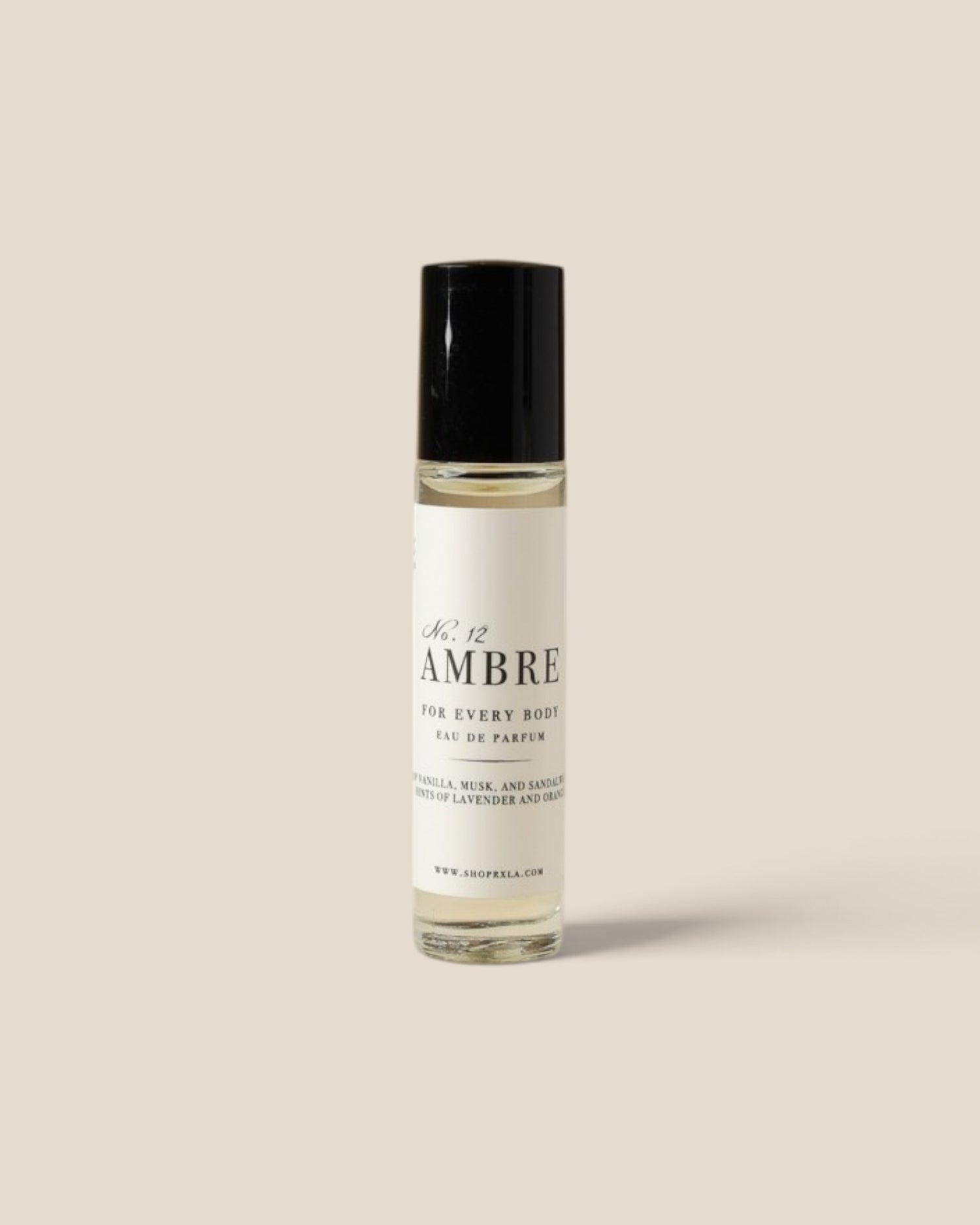 A roll-on perfume bottle with a black cap and a white label reading 'Ambre' , photographed against a solid beige background.