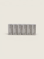Six small rectangular fragrance boxes standing upright in a row on a plain warm off-white background. The boxes are light gray with black text reading 'PURE FRAGRANCE' and a small monogram logo near the bottom.