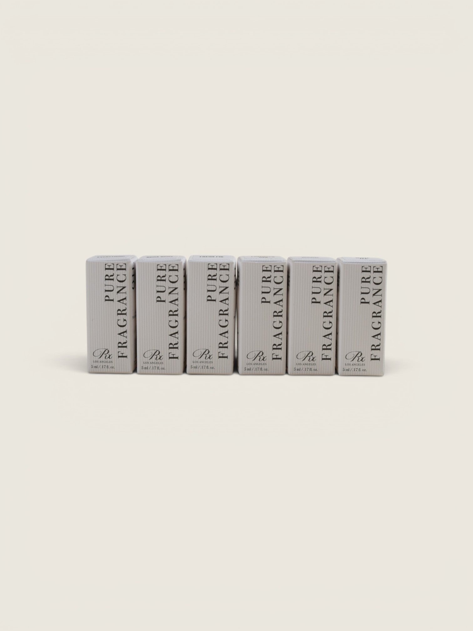 Six small rectangular fragrance boxes standing upright in a row on a plain warm off-white background. The boxes are light gray with black text reading 'PURE FRAGRANCE' and a small monogram logo near the bottom.