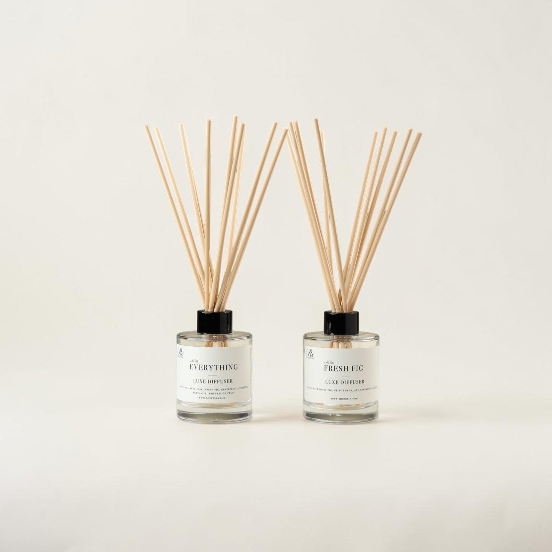 Two reed diffusers with clear glass bottles, white labels, and natural wooden reeds, set against a plain off-white background.
