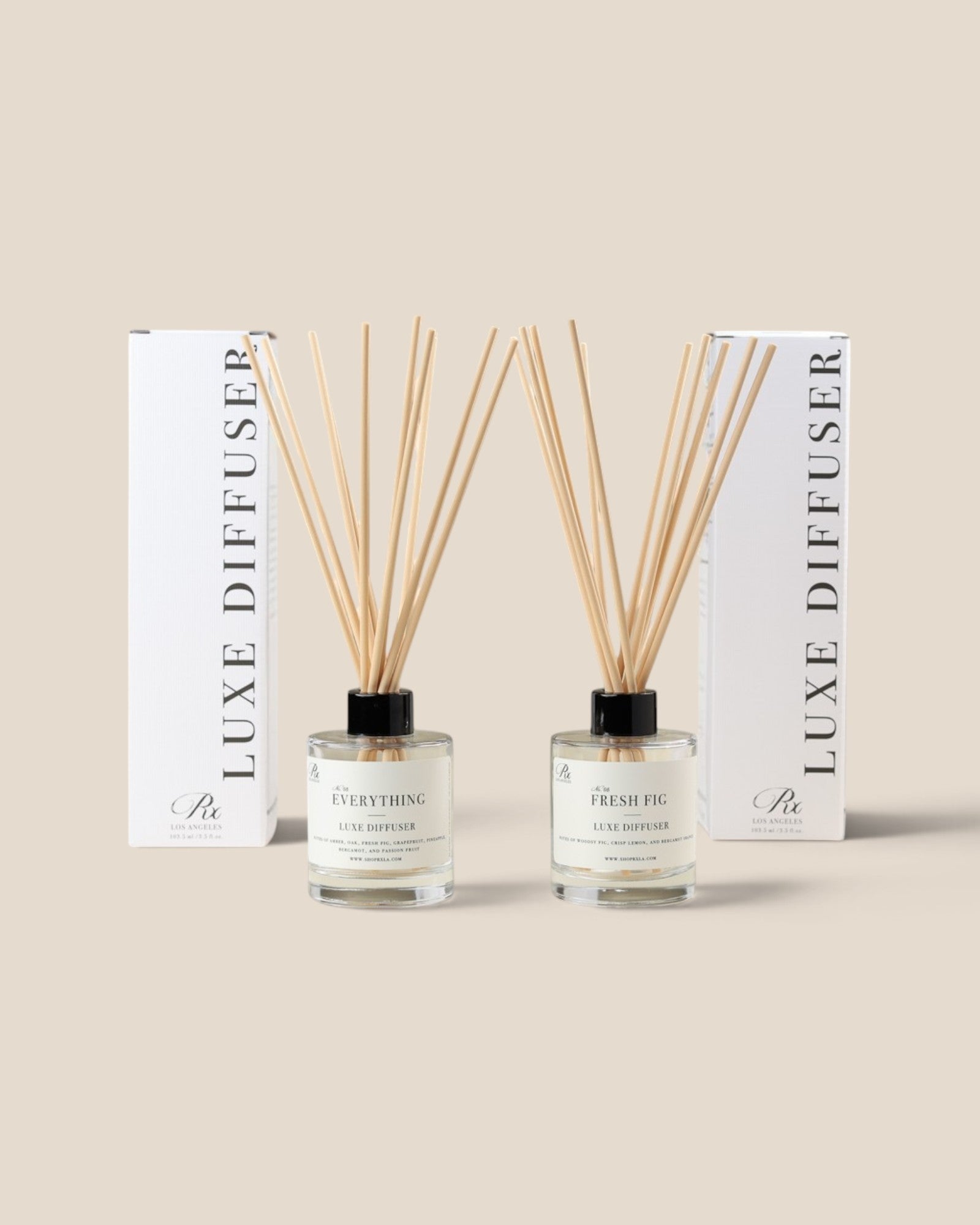 Two reed diffuser bottles with natural reed sticks and two tall white boxes labeled LUXE DIFFUSER, arranged on a warm beige background.