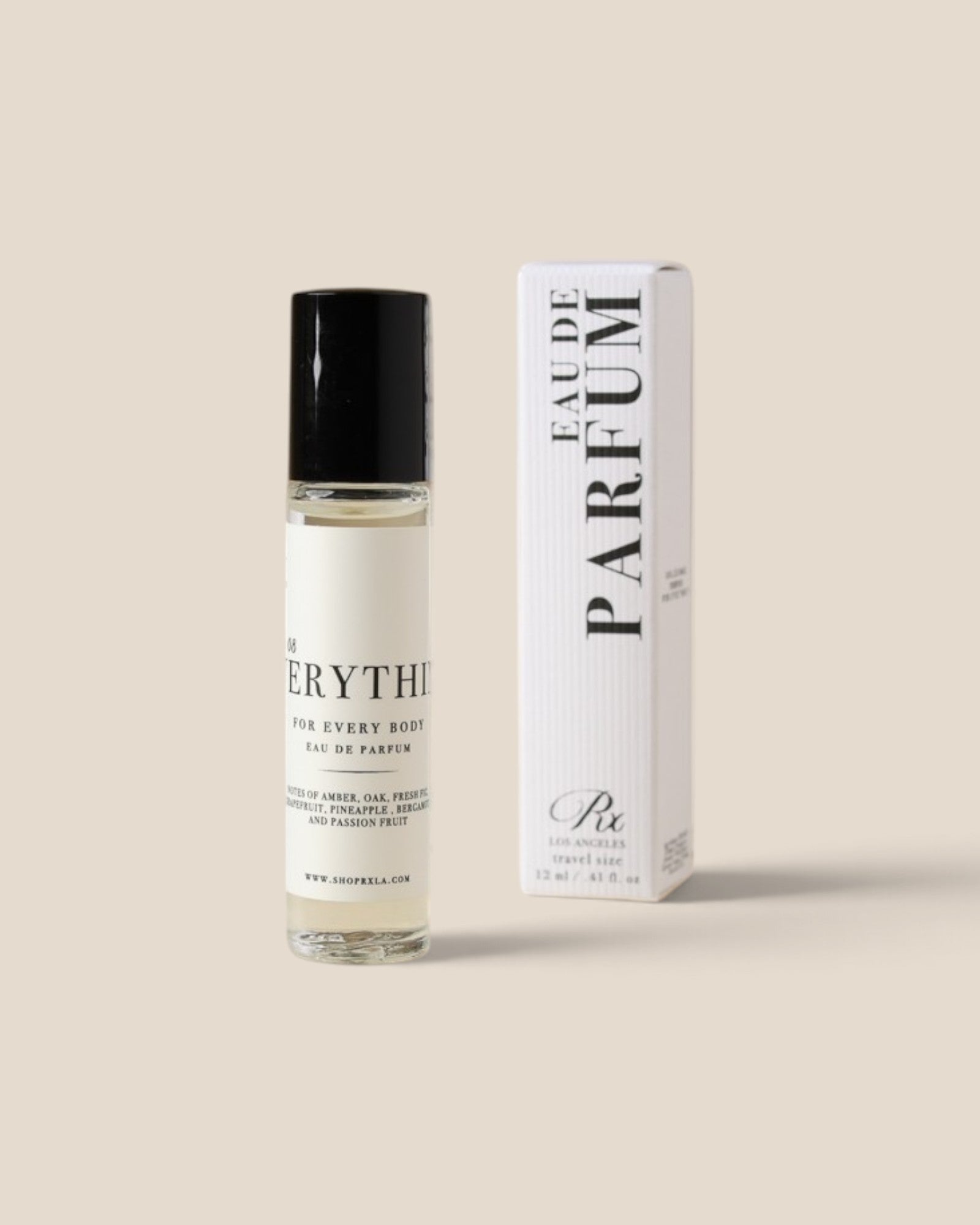 A clear glass roll-on perfume bottle with a black cap stands next to its white box packaging, both featuring black text, on a solid light beige background.