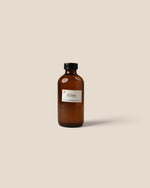 An amber glass bottle with a black cap and a white label reading 'HOMME', centered on a solid beige background.