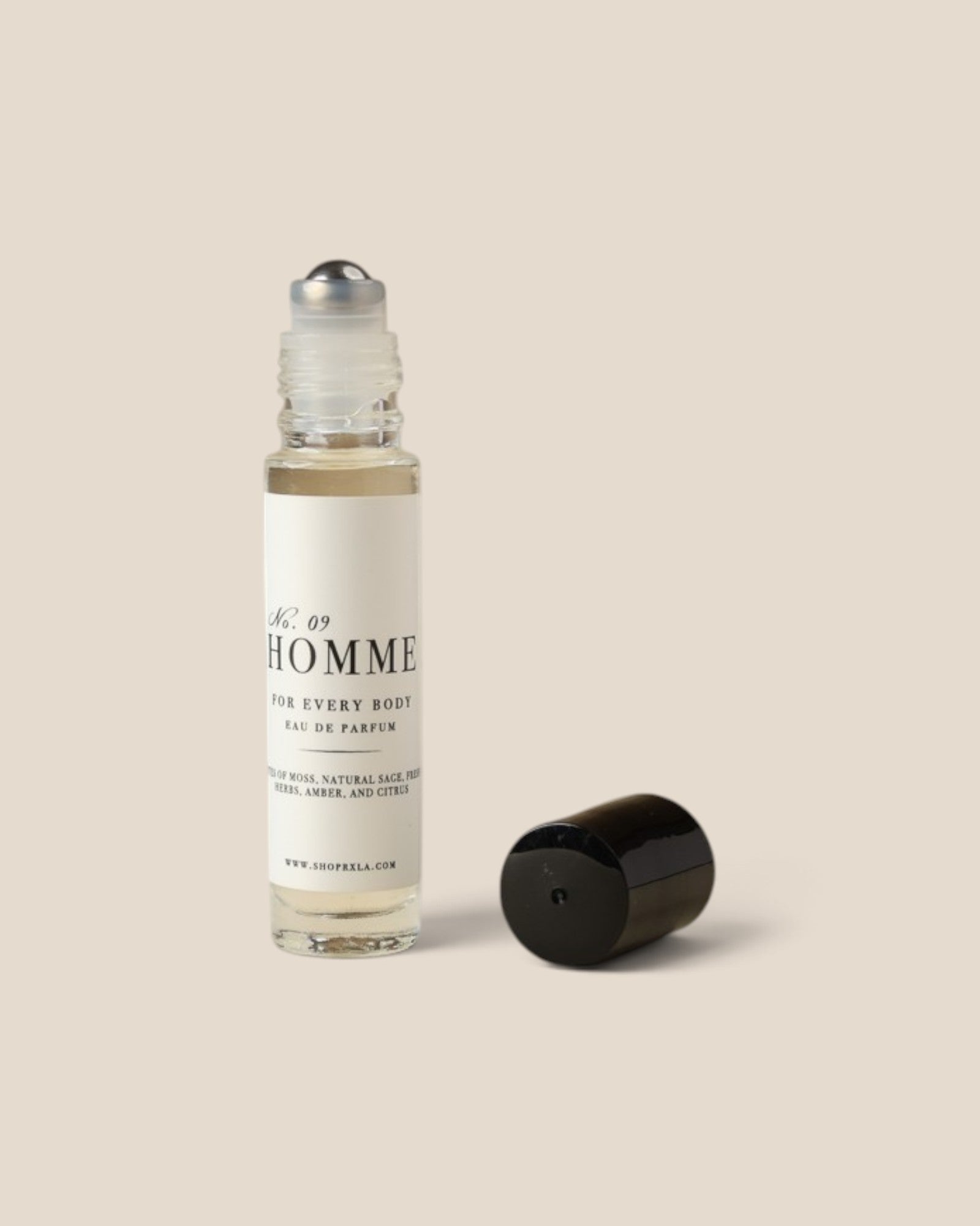 A clear glass rollerball perfume bottle with a white label reading 'HOMME' and a black cap placed beside it on a plain warm beige background.