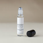 A clear glass rollerball perfume bottle with a white label reading 'SANTAL' and 'FOR EVERY BOTTLE EAU DE PARFUM', shown on a warm beige background with its black cap placed beside it.