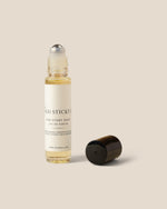 A clear glass rollerball bottle with pale yellow liquid and a cream label reading 'mango sticky rice' and 'FOR EVERY Boddy', shown next to its detached black cap on a warm beige background.