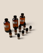 A set of amber glass bottles with black caps and white labels, including two dropper bottles and several small vials, arranged on a plain beige background.