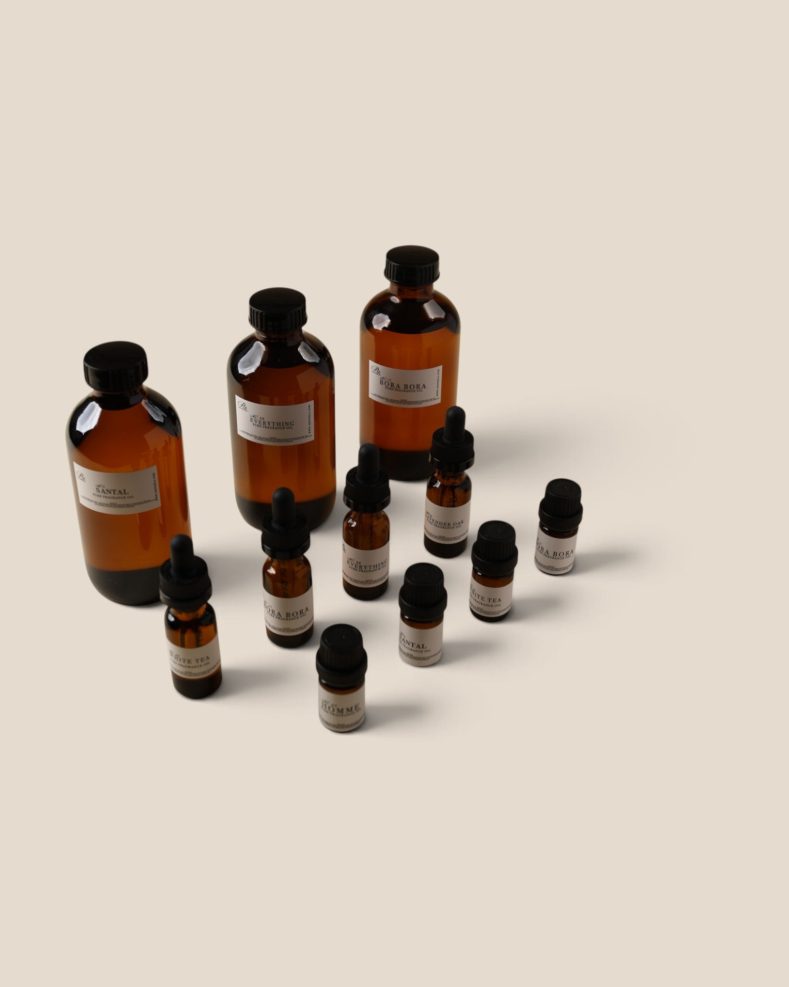 A set of amber glass bottles with black caps and white labels, including two dropper bottles and several small vials, arranged on a plain beige background.