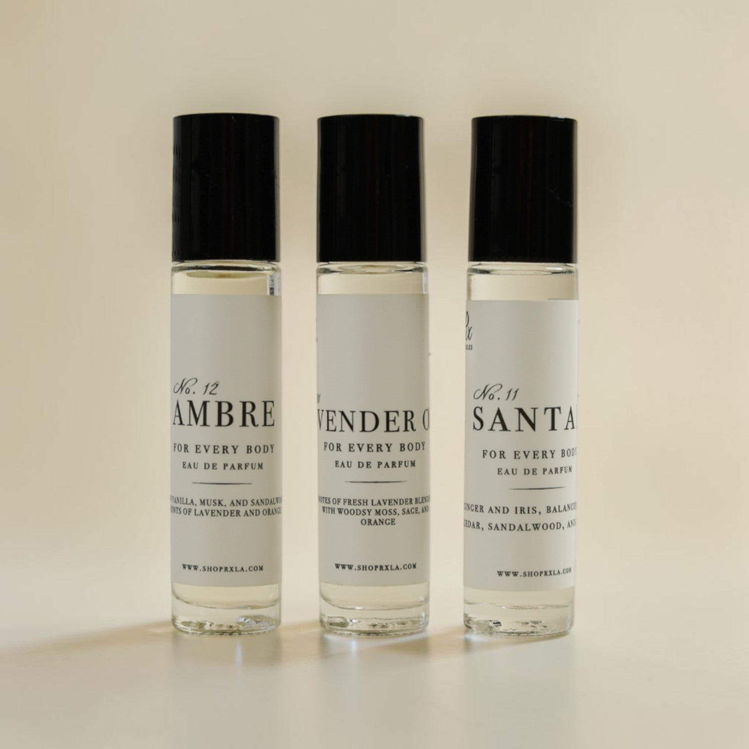 Three small clear perfume roller bottles with black caps and white labels, standing upright on a light beige background. The labels read No.