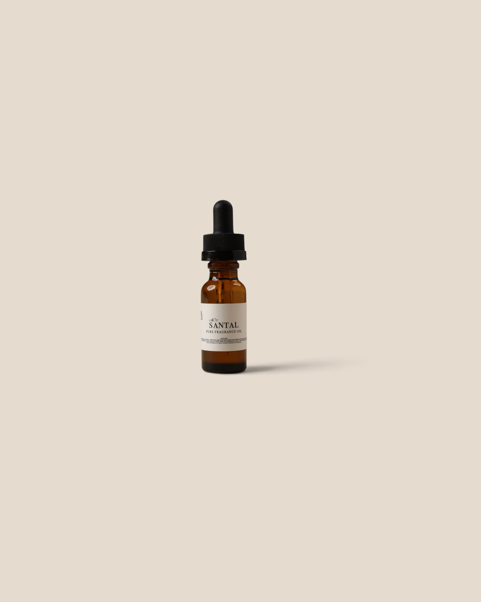 A small amber glass dropper bottle with a black rubber dropper cap and a white label reading SANTAL, centered on a plain warm beige background.