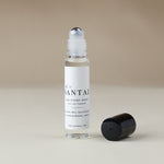 A clear glass rollerball perfume bottle with a white label reading 'SANTAL' and 'FOR EVERY BOTTLE EAU DE PARFUM', shown on a warm beige background with its black cap placed beside it.