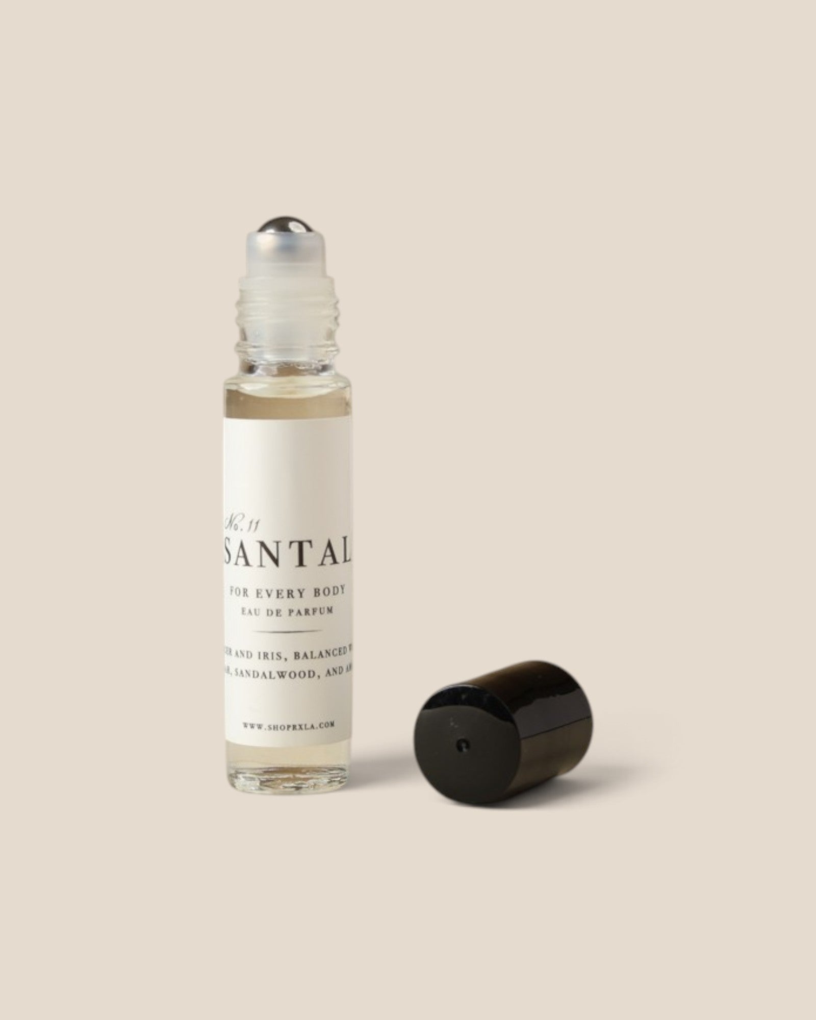A clear glass rollerball bottle with a white label reading 'SANTAL' and 'FOR EVERY BODY', shown with its black cap placed beside it on a plain warm beige background.